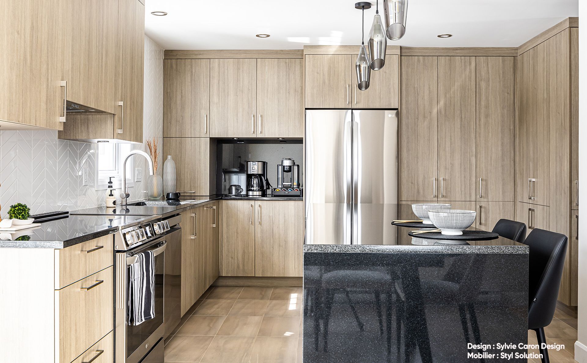 Cuisine moderne avec armoires en bois clair, appareils électroménagers en acier inoxydable et îlot central avec comptoir foncé.