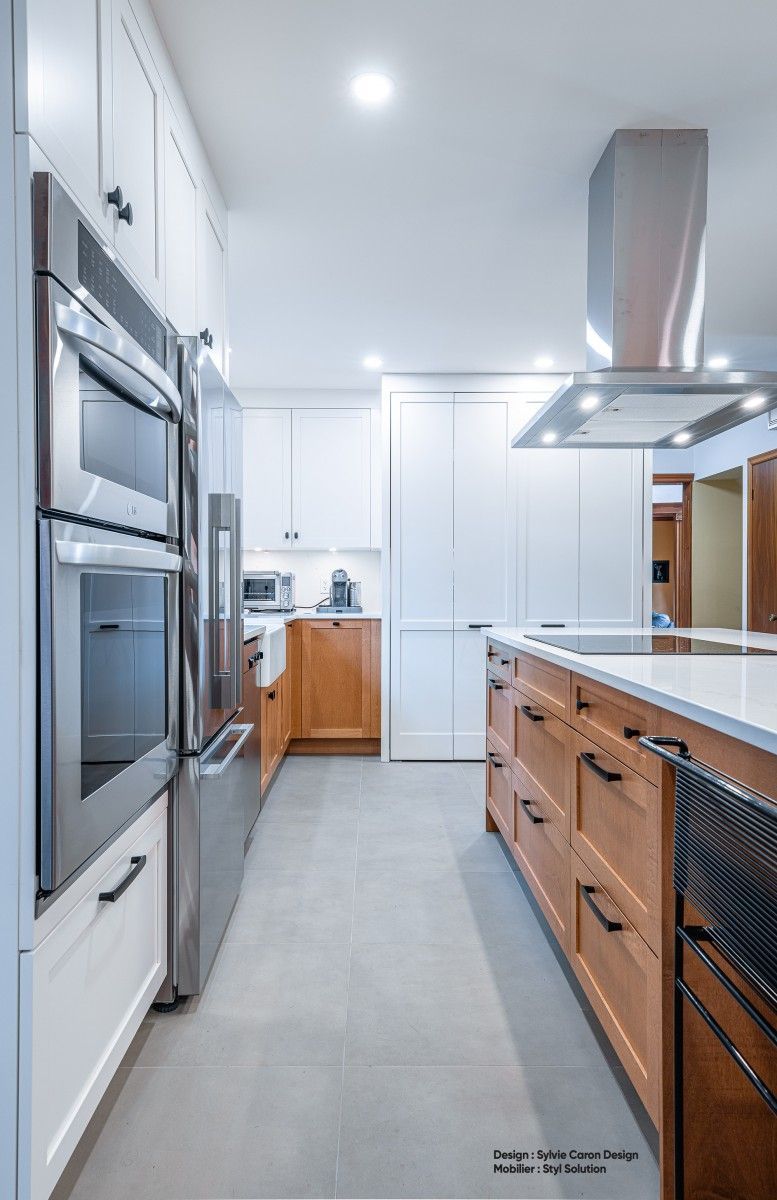 Cuisine moderne avec appareils électroménagers en acier inoxydable, armoires blanches et îlot en bois.