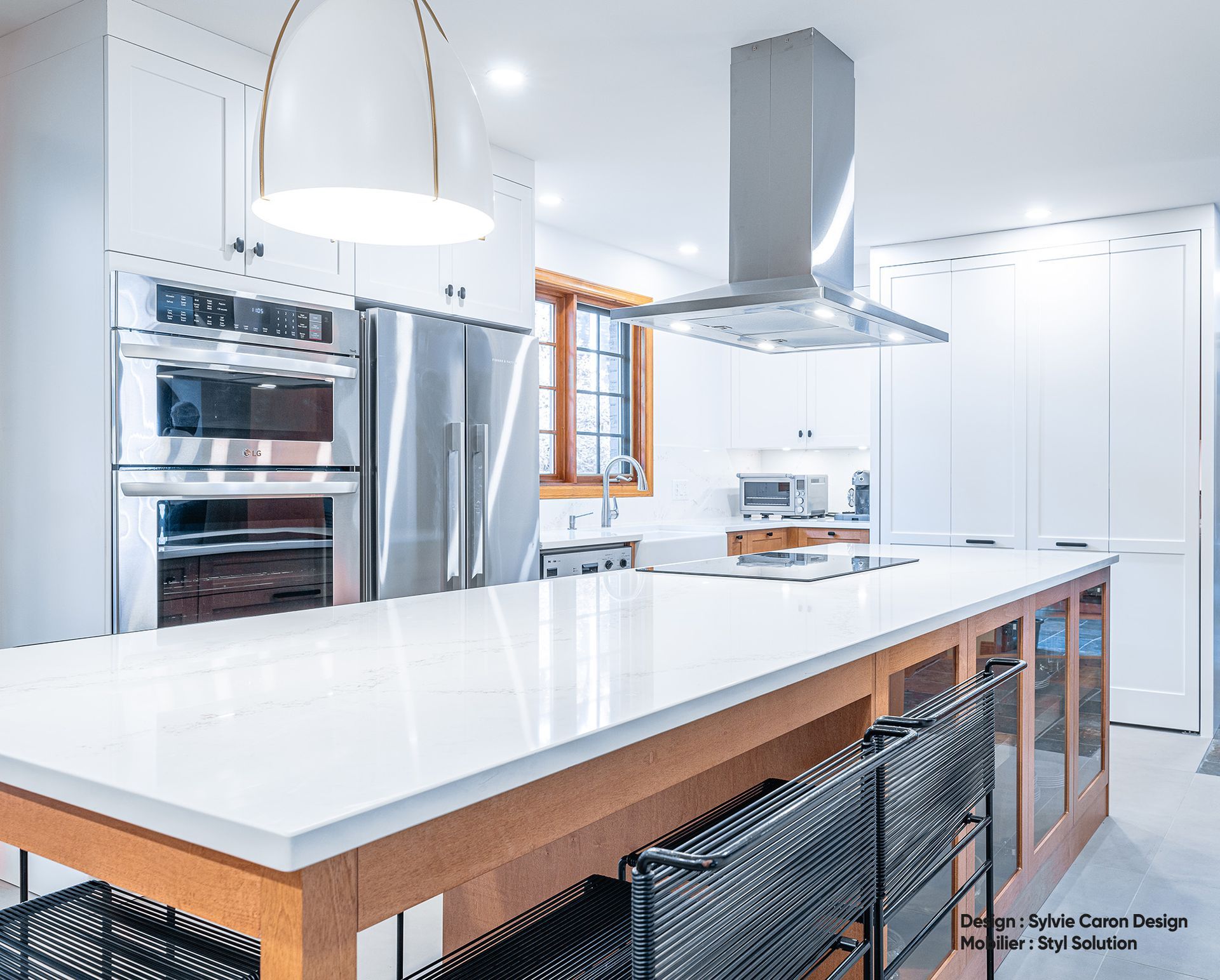 Cuisine moderne avec armoires blanches, électroménagers en acier inoxydable et grand îlot avec places assises.