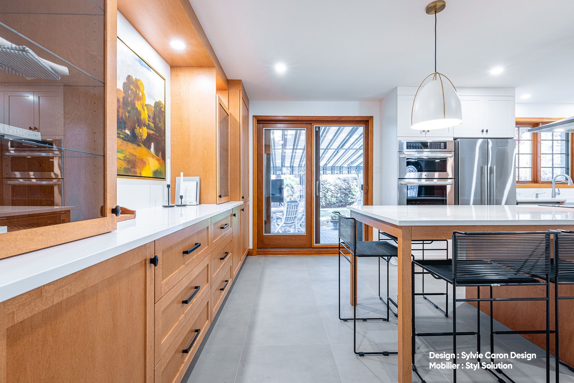 Cuisine moderne avec placards en bois, plans de travail blancs et îlot central avec sièges.