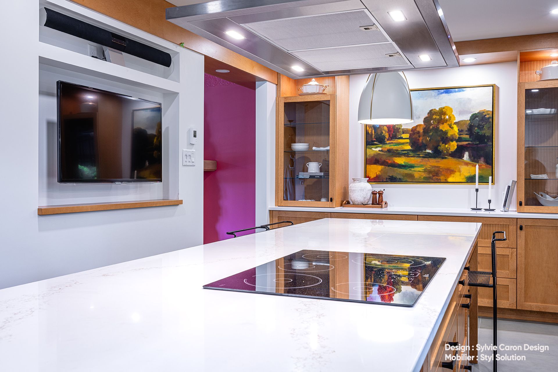 Cuisine moderne avec îlot central blanc, plaque de cuisson, œuvres d'art, placards en bois et télévision murale.