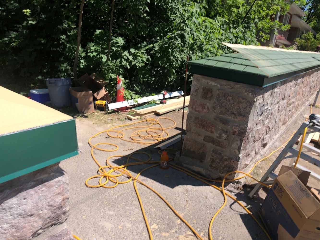 Construction d'un mur en pierre à l'aide d'outils, d'un câble électrique et de bois d'œuvre, en extérieur.