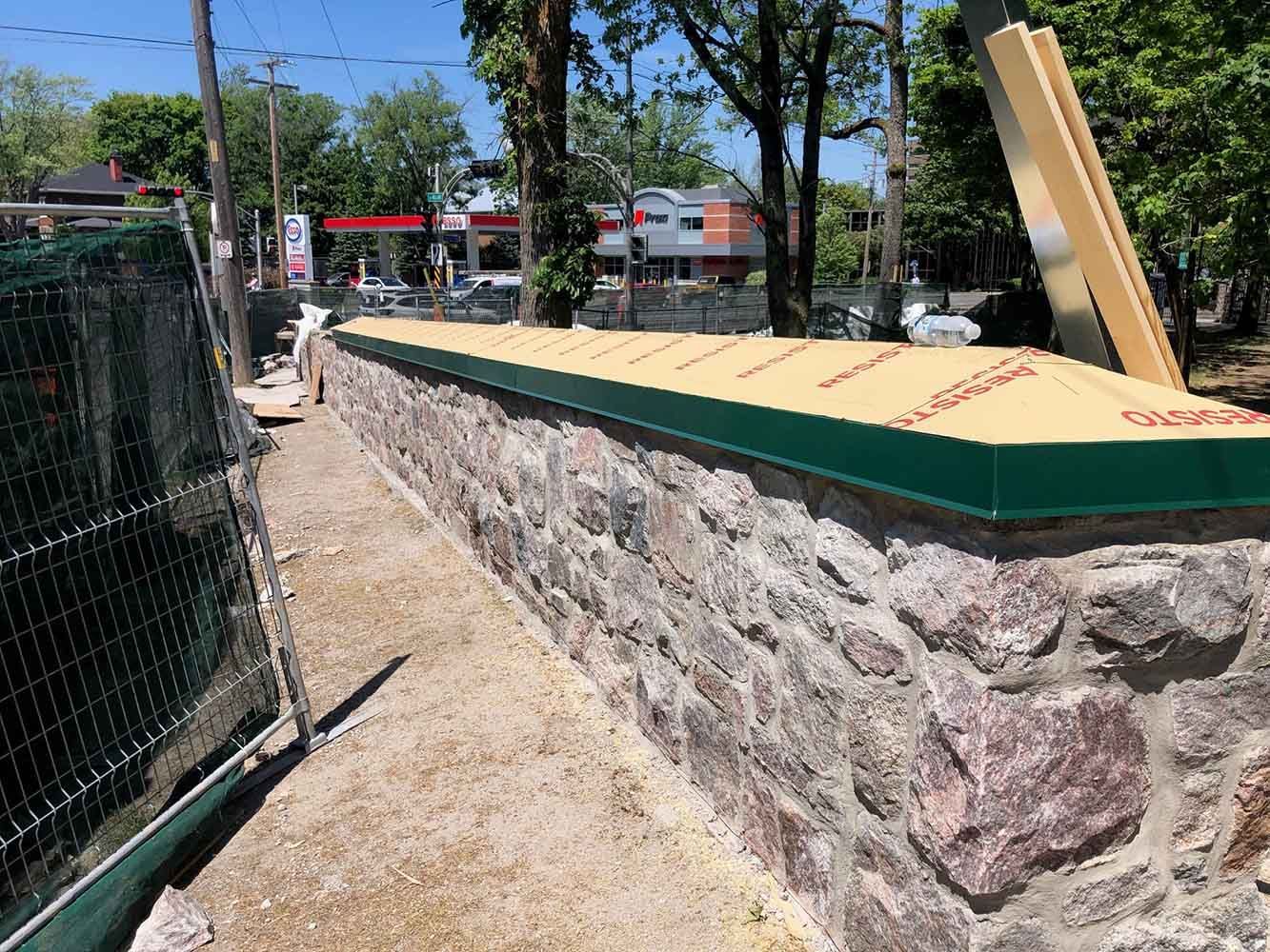 Mur en pierre à sommet vert, matériaux de construction à proximité.