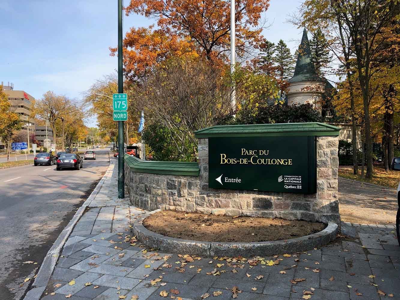 Panneau indiquant le parc des Rapides, pointant à gauche. Allée pavée longeant une route avec des voitures, feuillage d'automne.