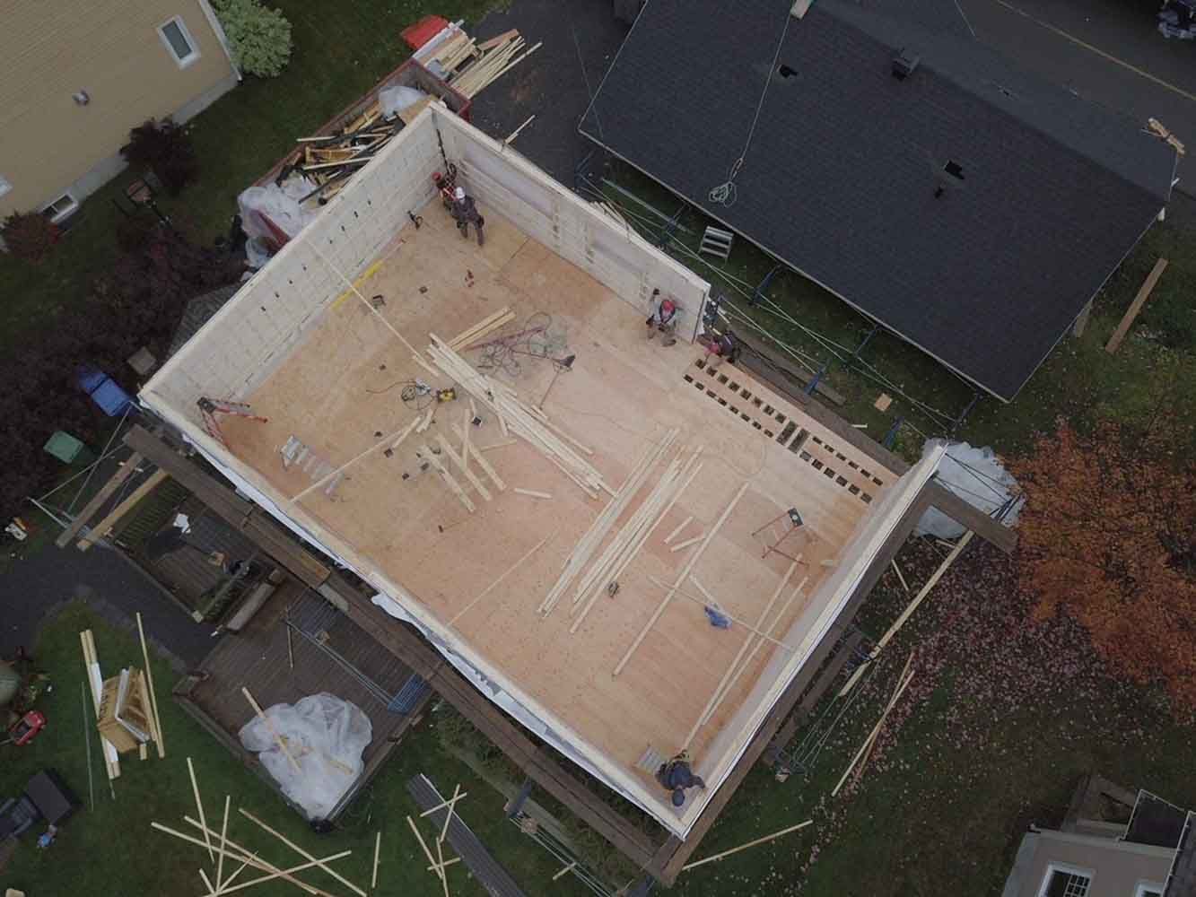 Vue aérienne d'un bâtiment en construction, des ouvriers assemblant des murs en bois.