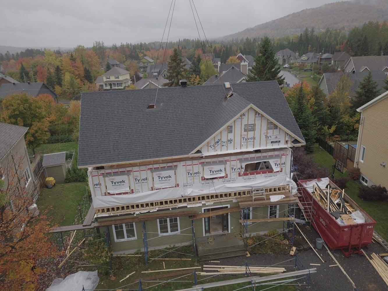 Maison en construction avec bâches et échafaudages ; feuillage d'automne et autres maisons en arrière-plan.