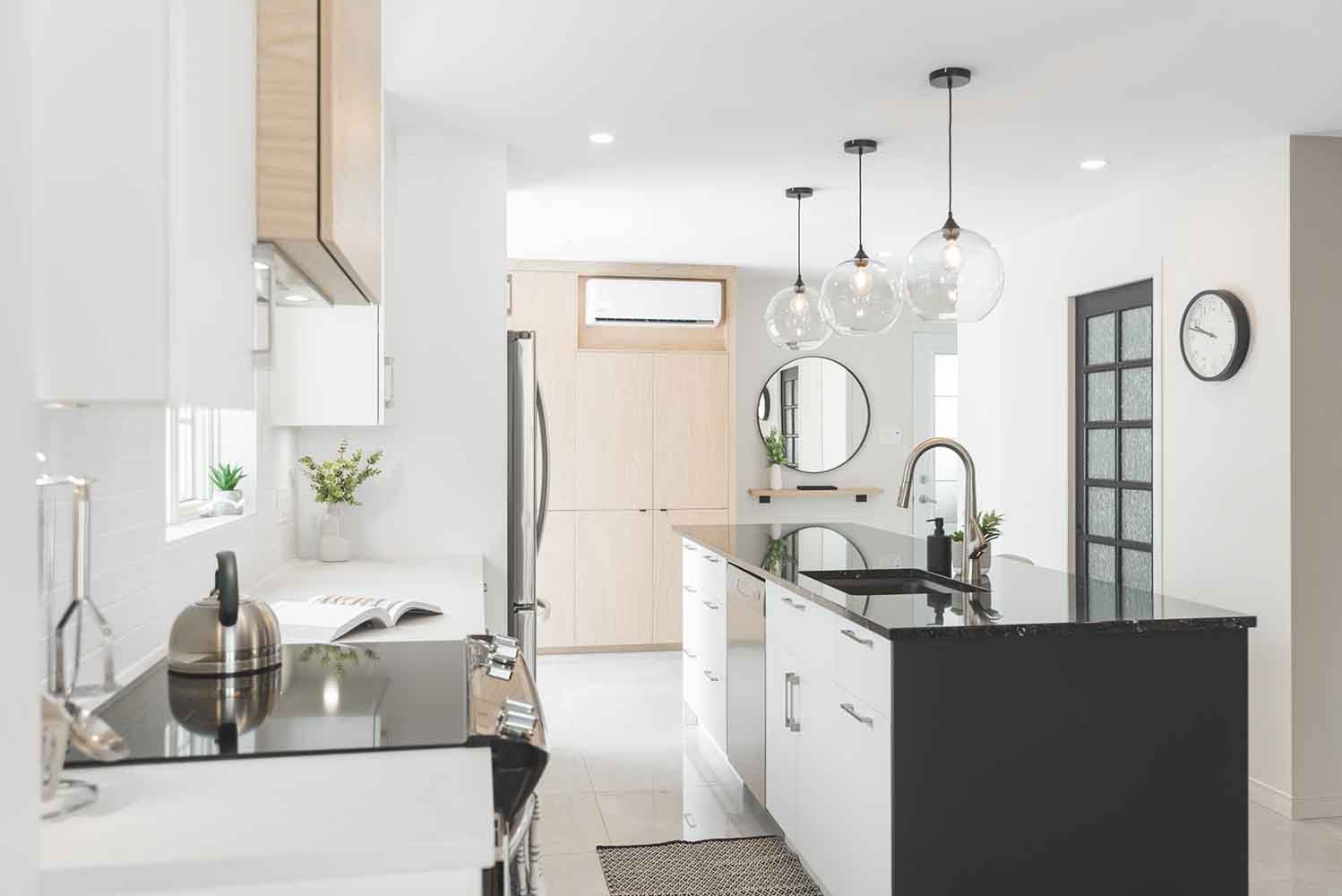 Cuisine moderne avec placards noirs et blancs, îlot central et suspensions lumineuses.