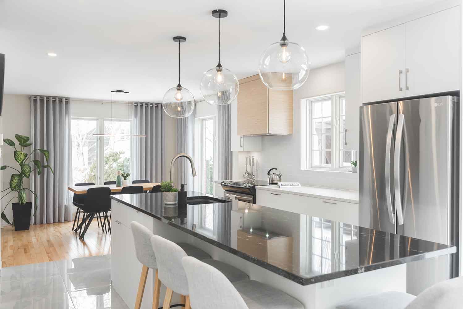 Cuisine moderne avec îlot central noir, appareils électroménagers en acier inoxydable et suspensions lumineuses.