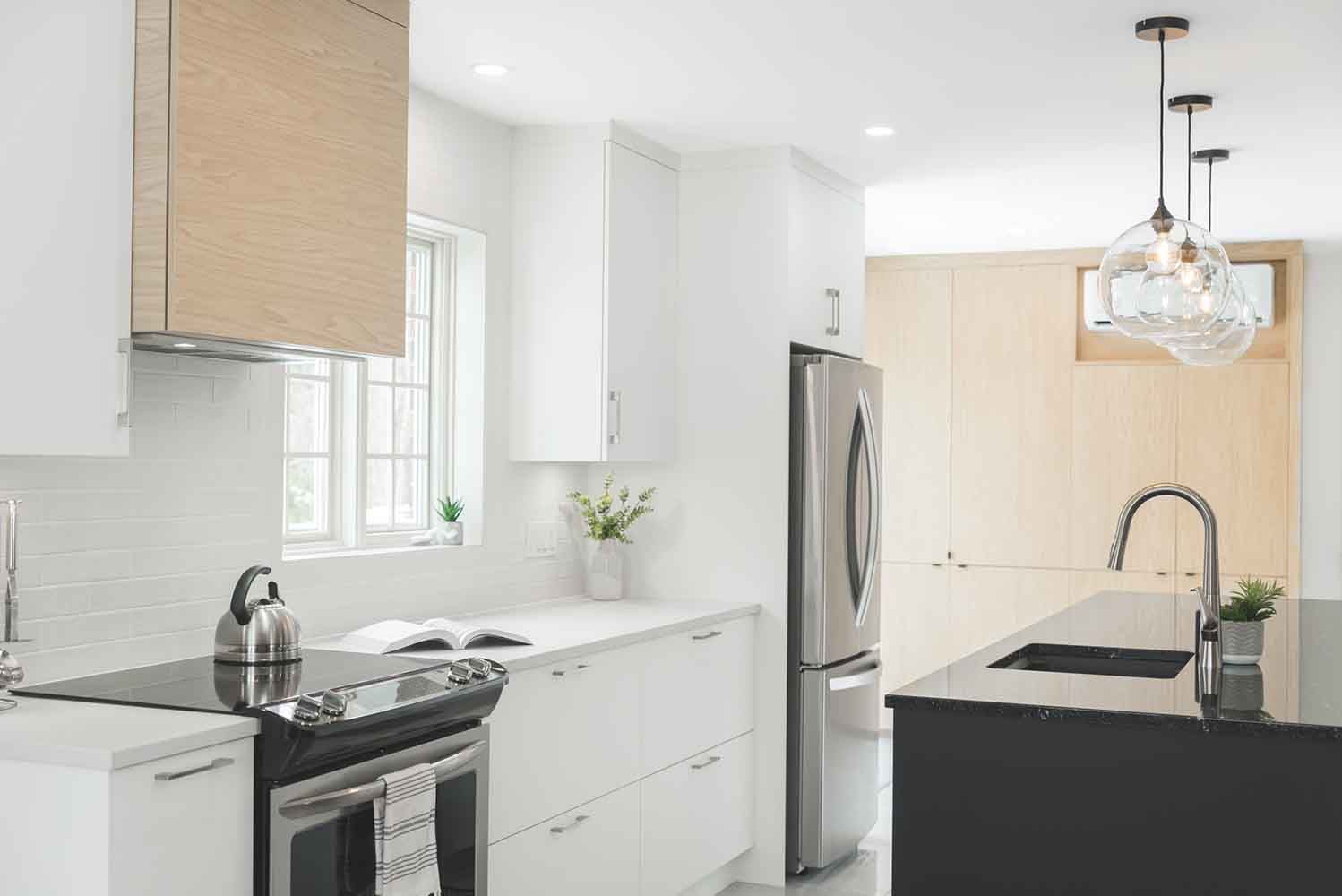Cuisine moderne avec armoires blanches, électroménagers en acier inoxydable et îlot noir.