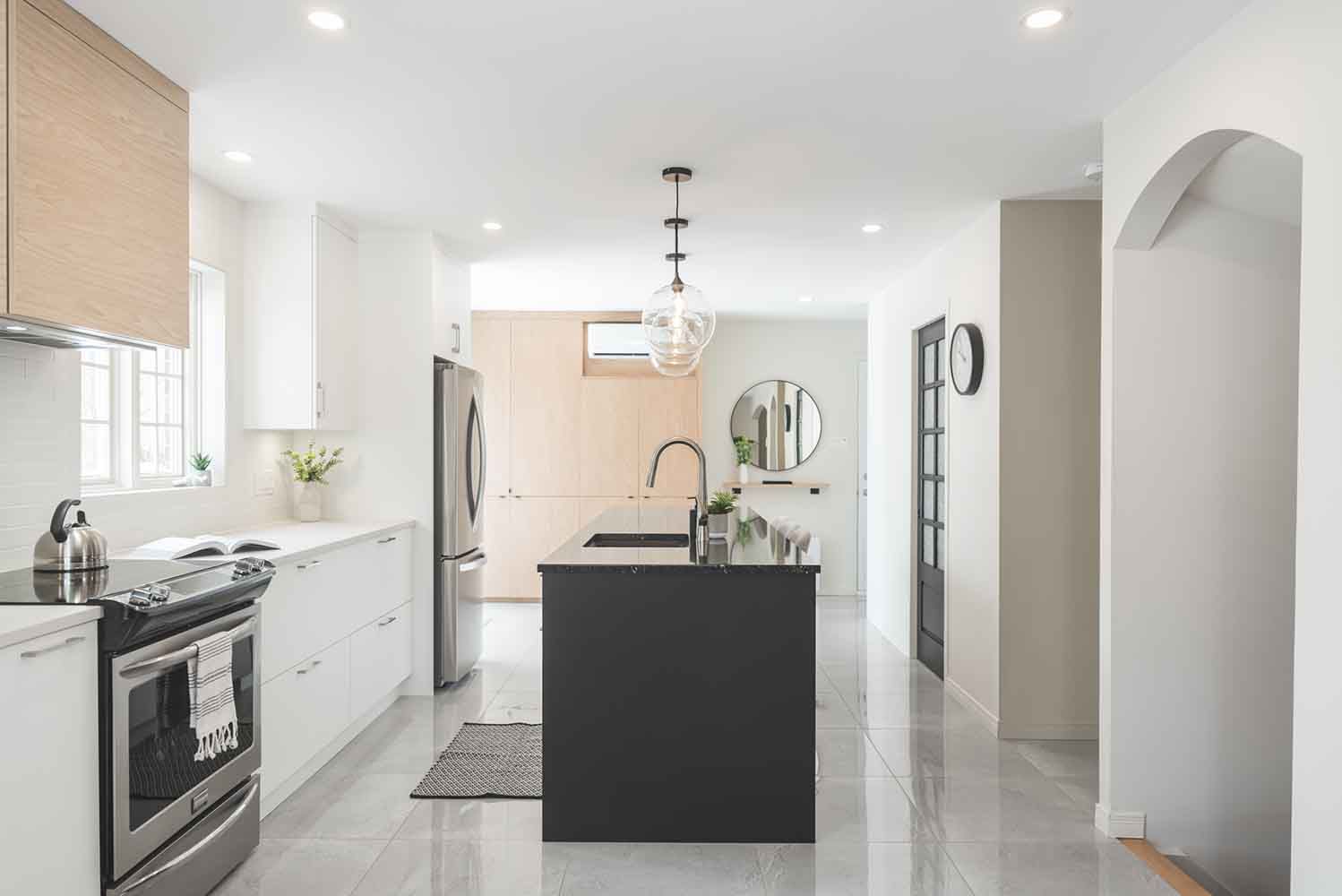 Cuisine moderne avec armoires blanches, îlot noir, appareils électroménagers en acier inoxydable et éléments en bois.