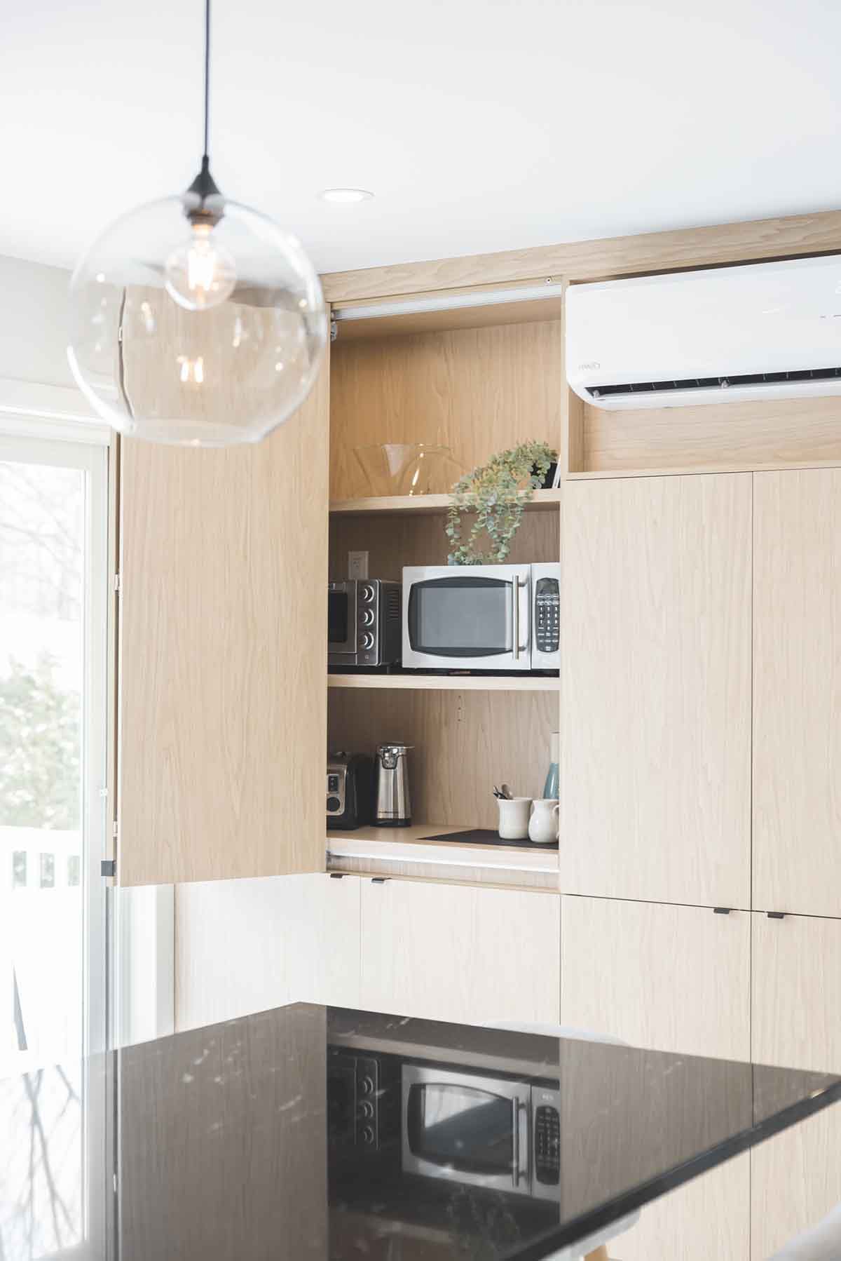 Cuisine moderne avec placards en bois clair, micro-ondes intégré et grande suspension lumineuse en verre.