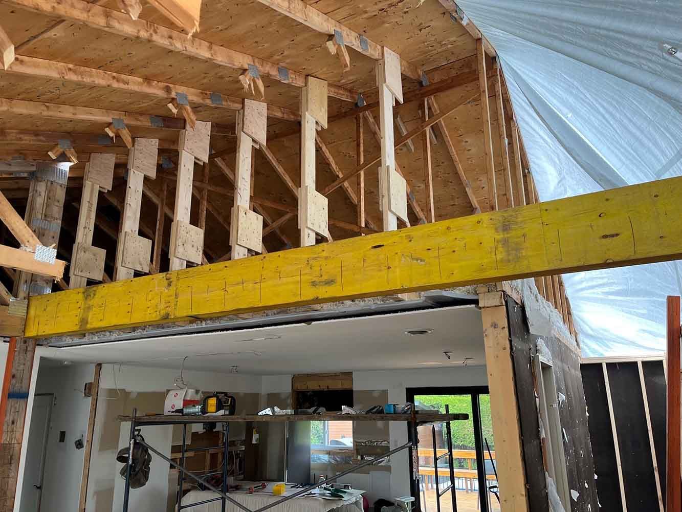 Chantier de construction avec charpente en bois apparente et poutre de soutien jaune.