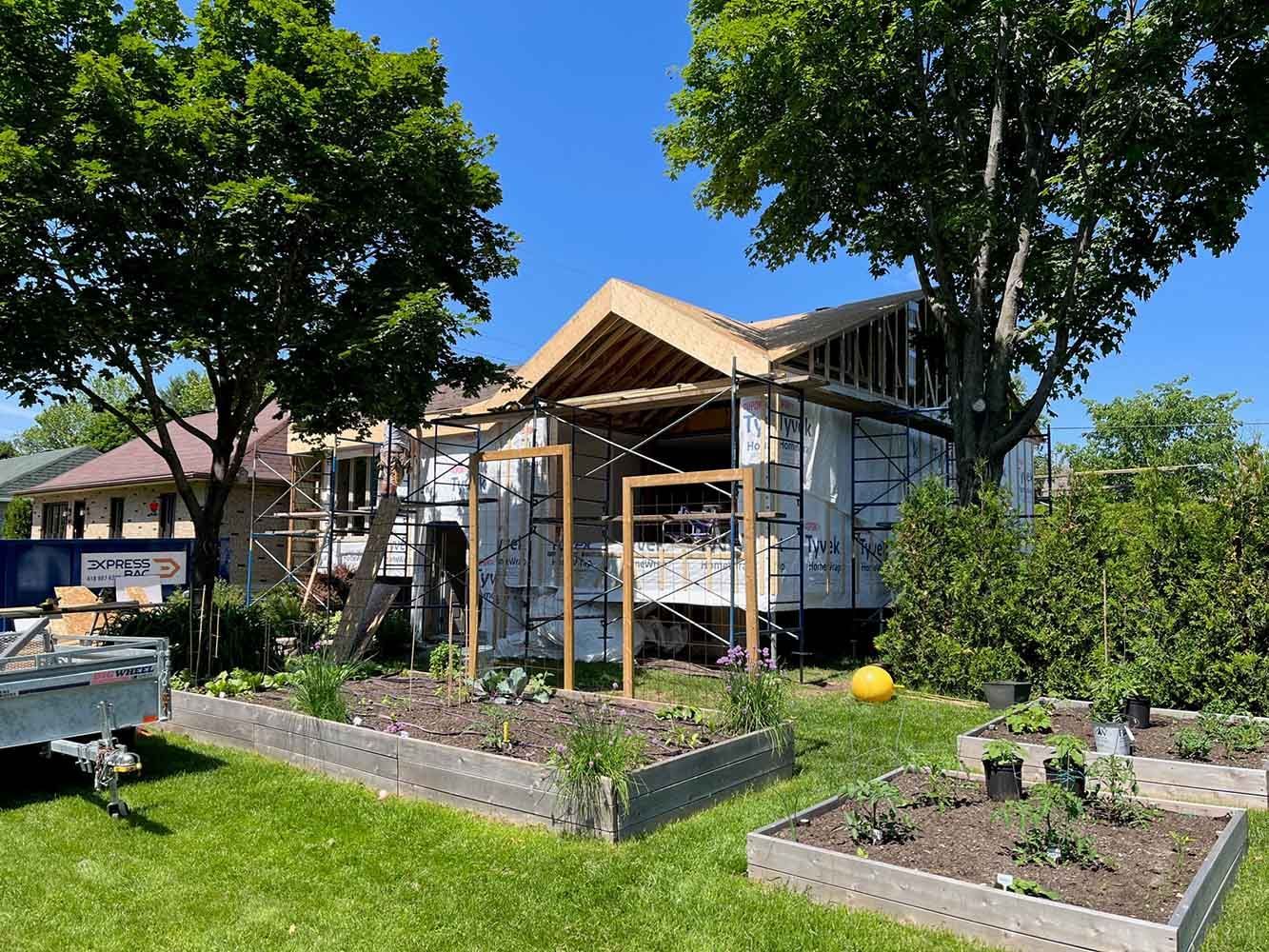 Maison en construction, avec ossature bois et échafaudages. Jardinières surélevées à l'avant.