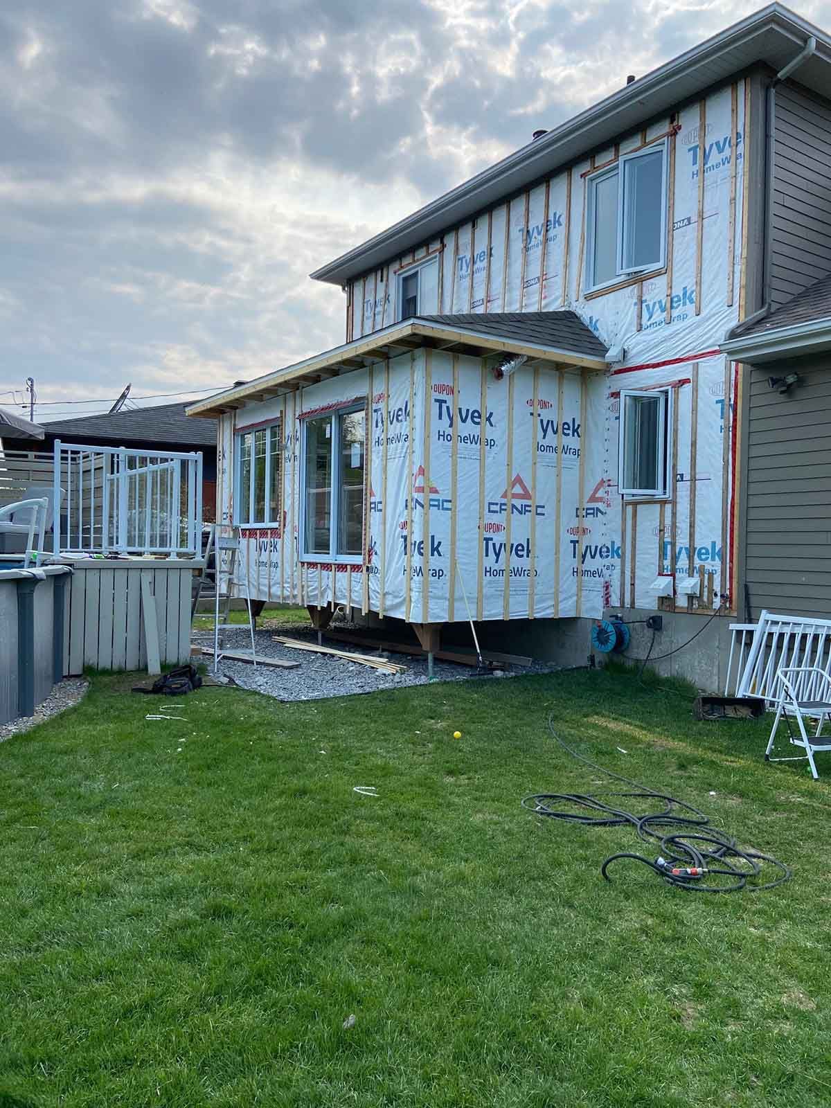 Vue arrière d'une maison en construction, avec un revêtement Tyvek et une charpente apparente.