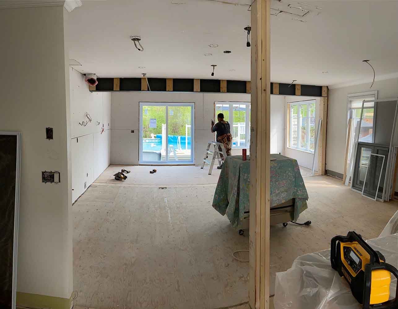 Intérieur d'une pièce en construction, avec une personne travaillant près d'une porte coulissante en verre.
