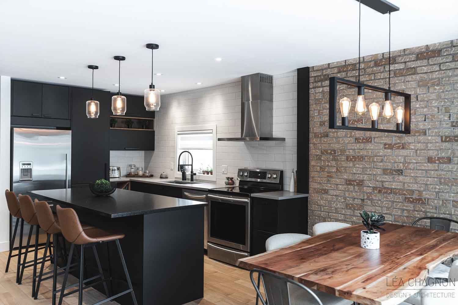 Cuisine moderne avec placards noirs, îlot central, mur en briques apparentes et table en bois.