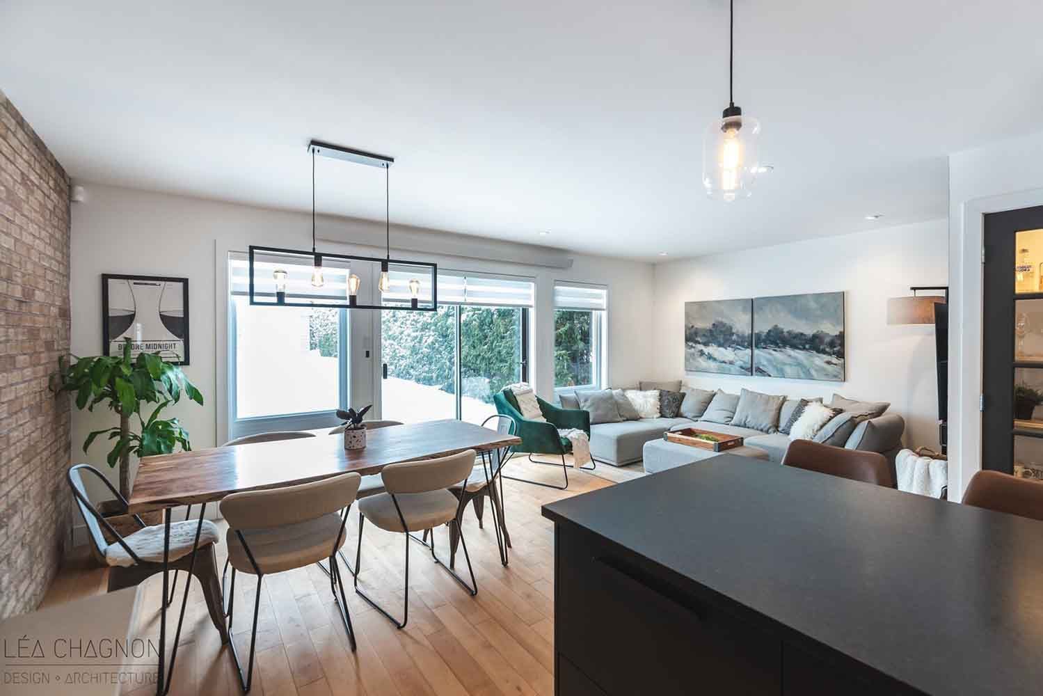 Espace de vie ouvert comprenant un coin repas, un îlot de cuisine et un canapé d'angle ; un mur d'accent en briques et une vue sur la neige à l'extérieur.