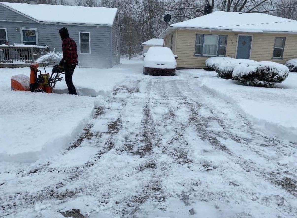 A man is using a snow blower to clear a driveway.