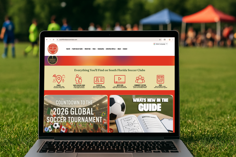 Laptop displaying a soccer tournament website on grass, with blurred soccer players in the background.