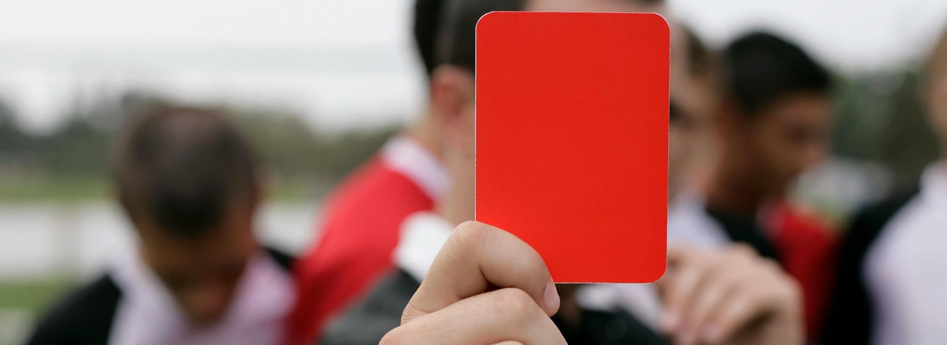 A hand holds up a red card, with blurred figures of athletes in the background.