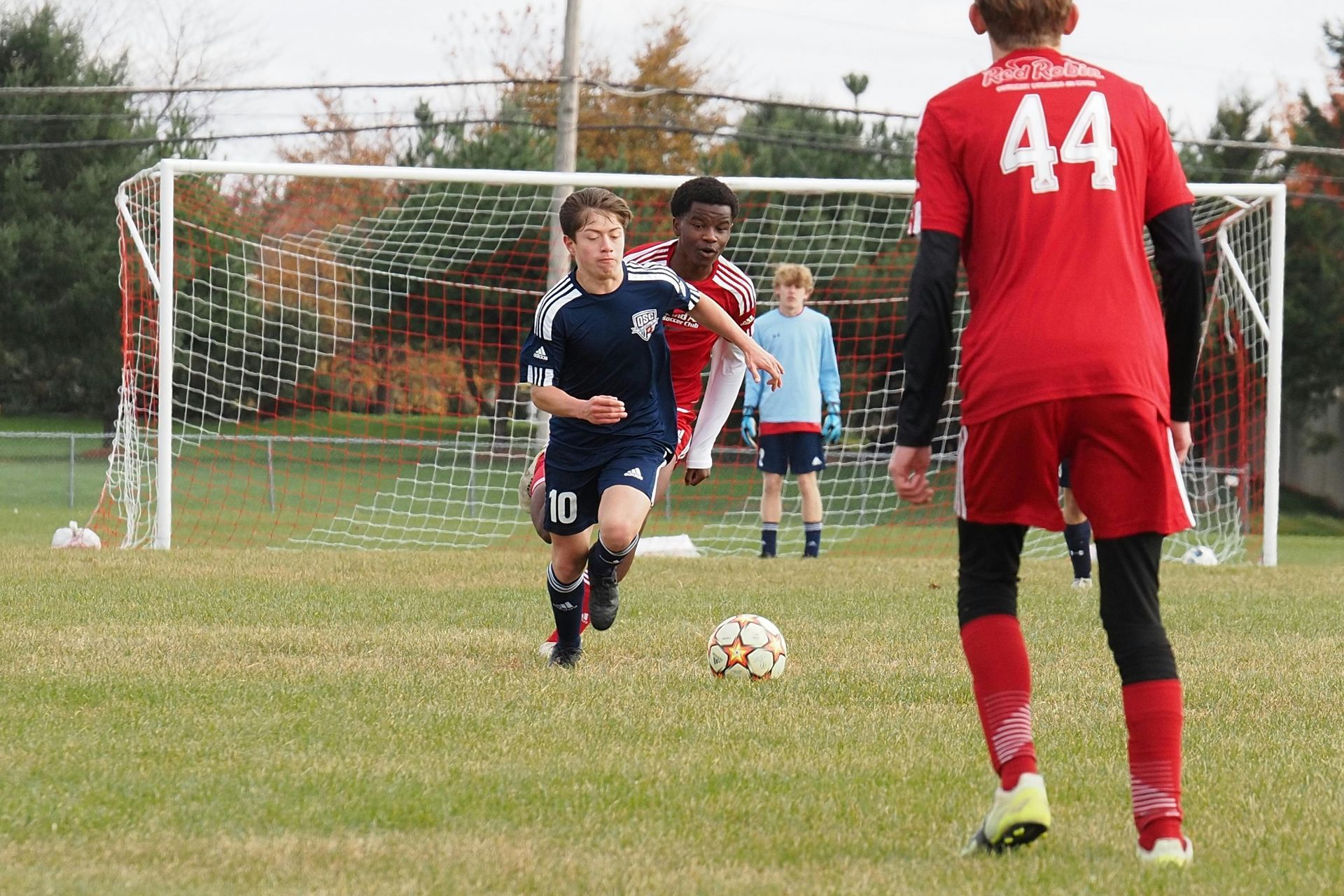 Soccer game: Player in blue runs with the ball toward the goal. Red team player defends.