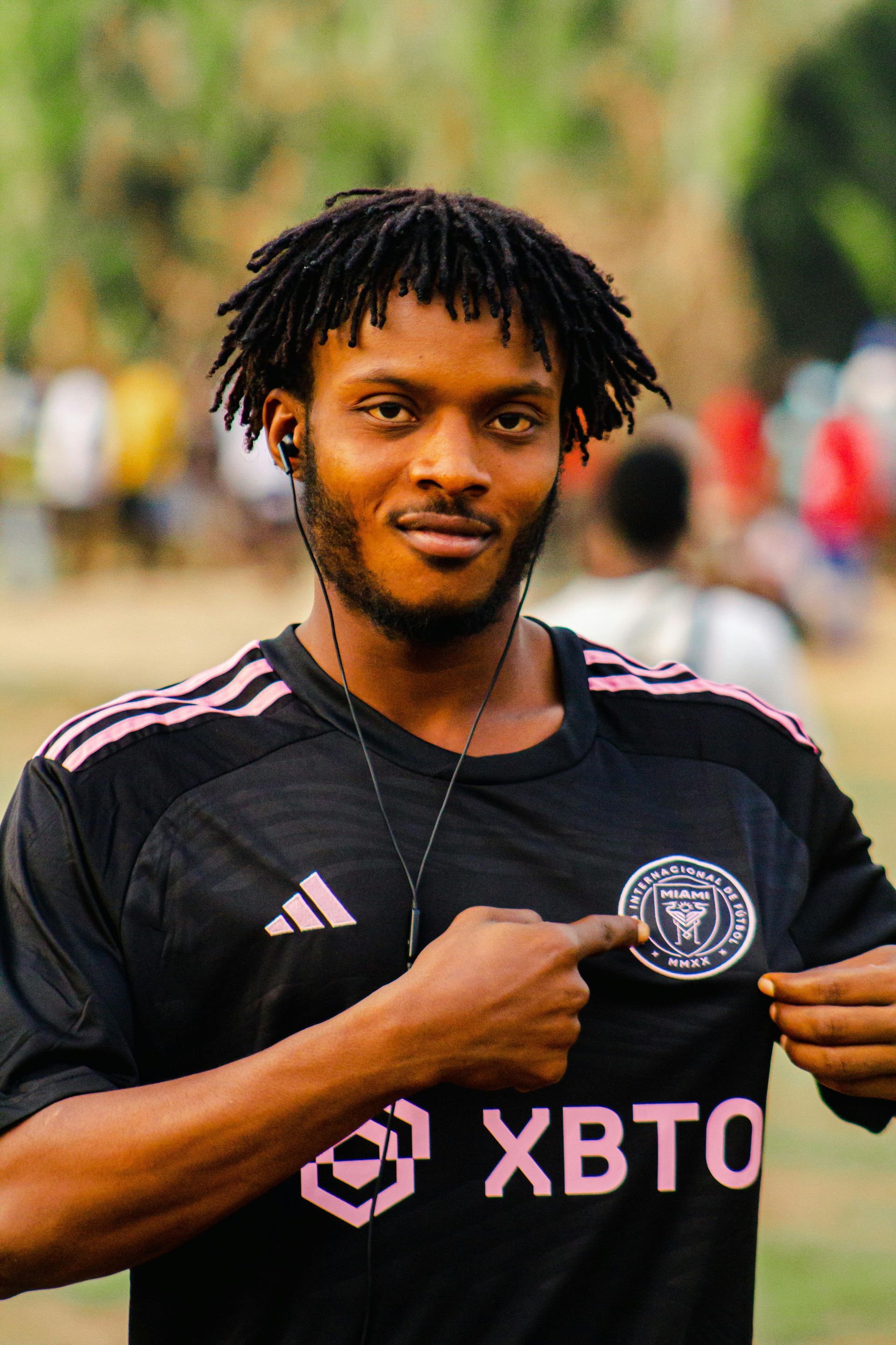 Man wearing black soccer jersey with pink stripes points at team logo.