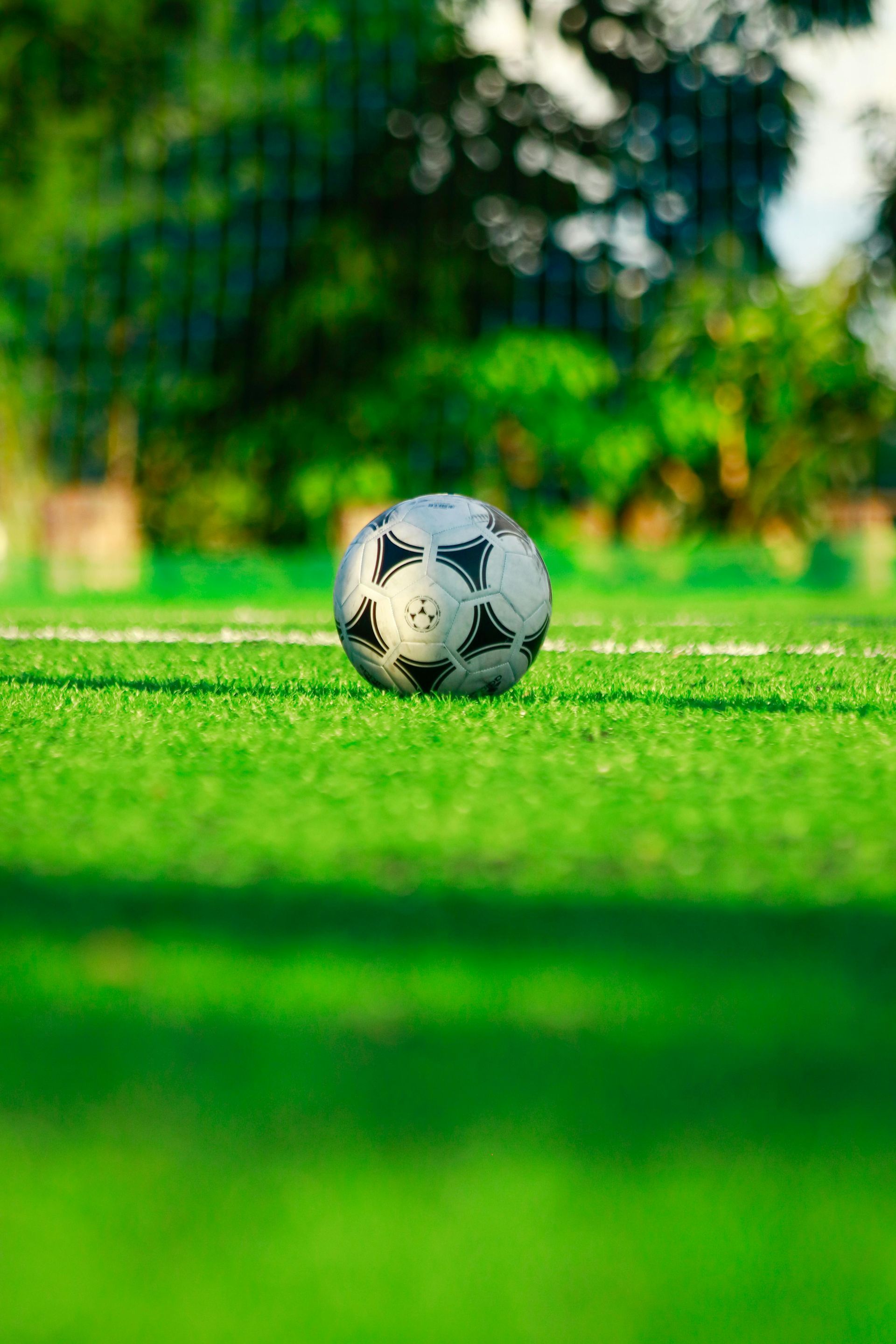 Soccer ball on green artificial turf field. Trees in the blurry background.