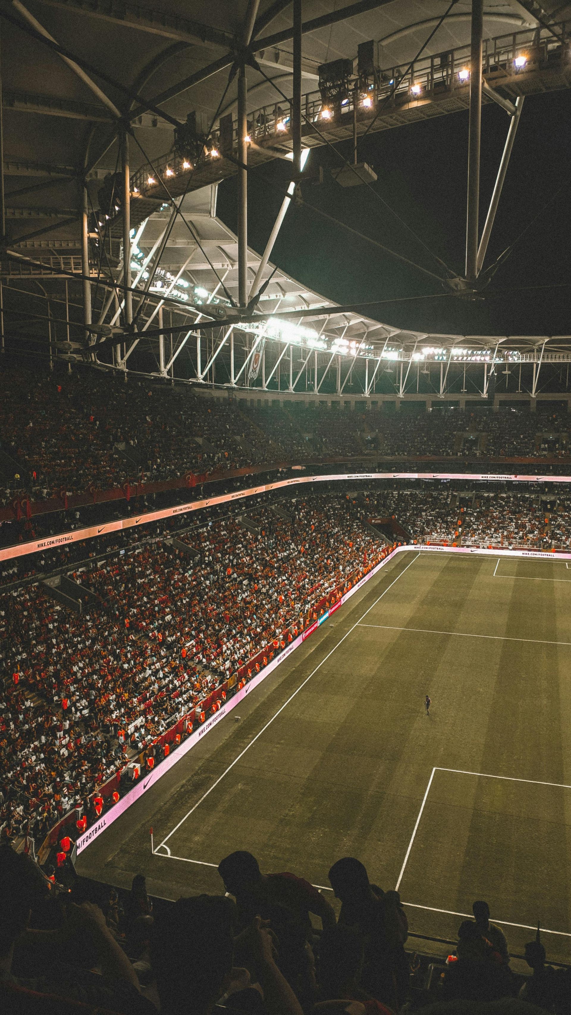 Football stadium at night, packed stands, green field, bright lights overhead.