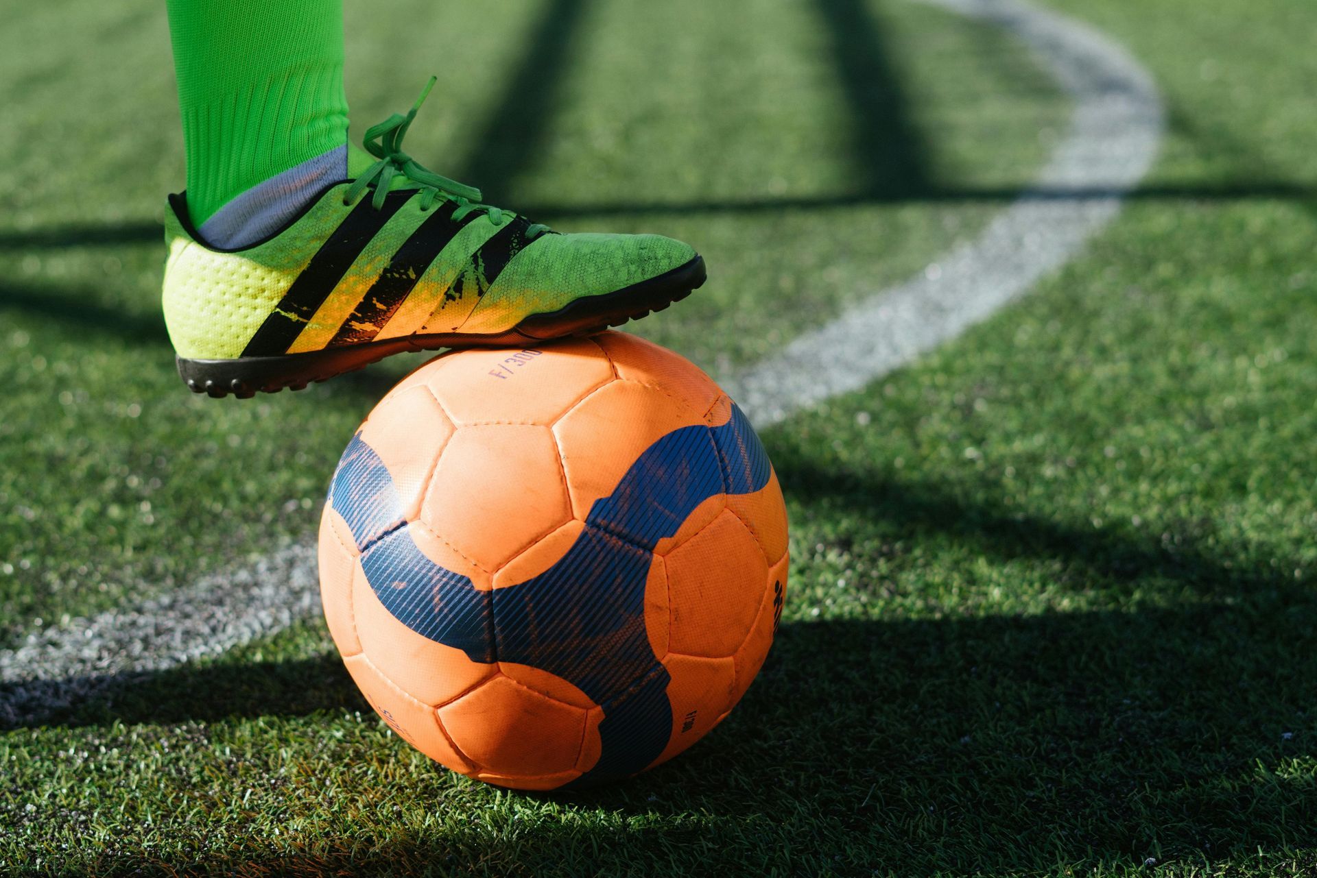 Soccer cleat on an orange soccer ball on a green field.