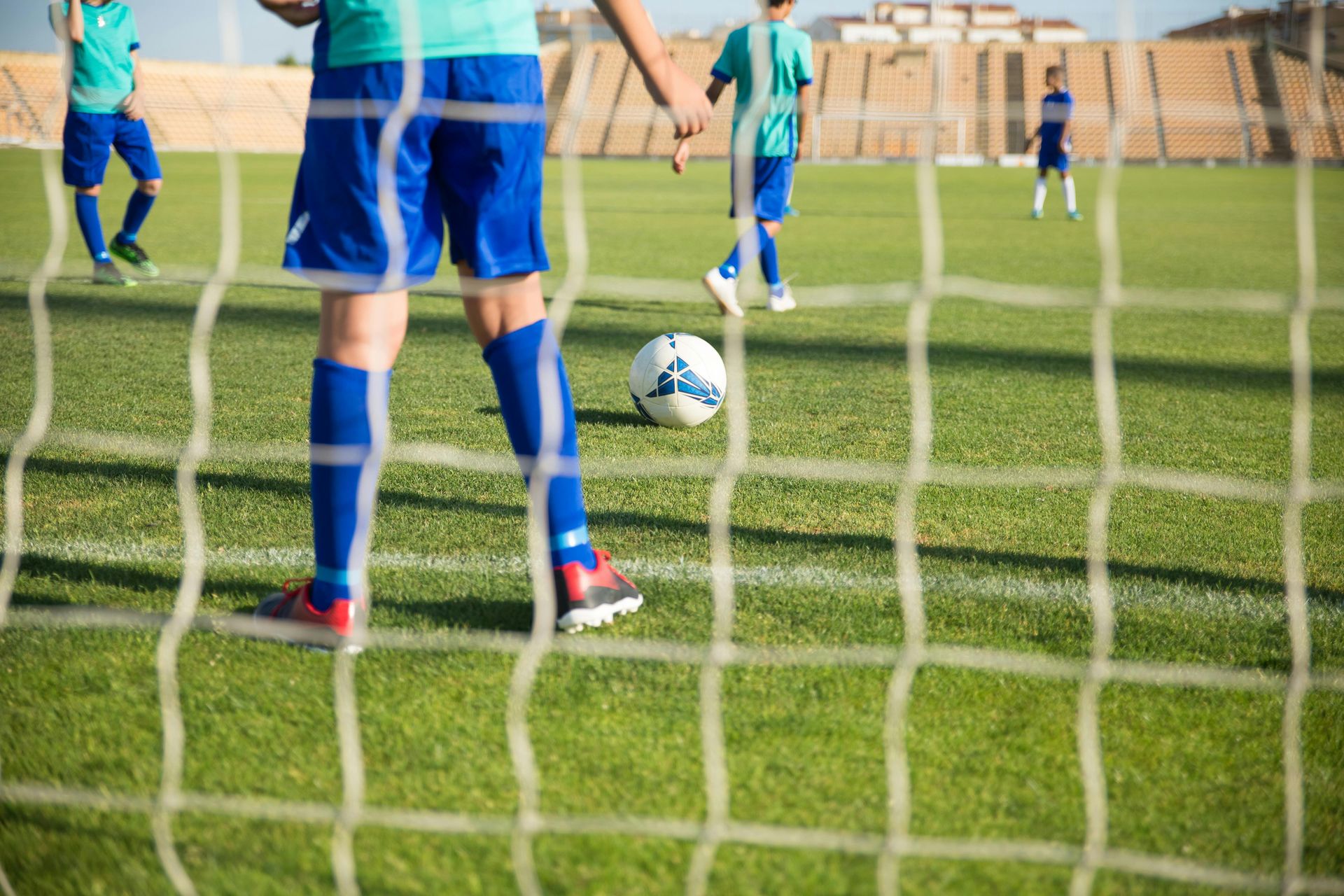 Soccer players on a green field; ball near the net, ready to be kicked.