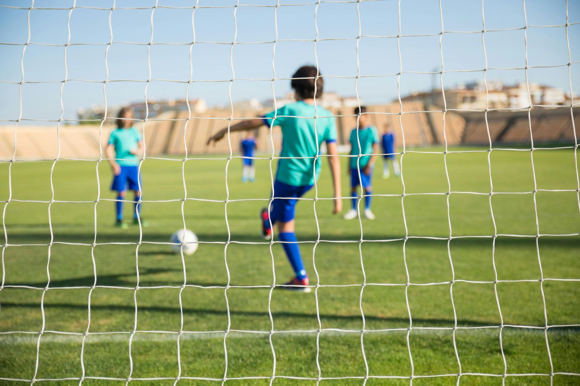 Soccer player kicking ball towards the goal. Other players in the background. Green field, blue sky.