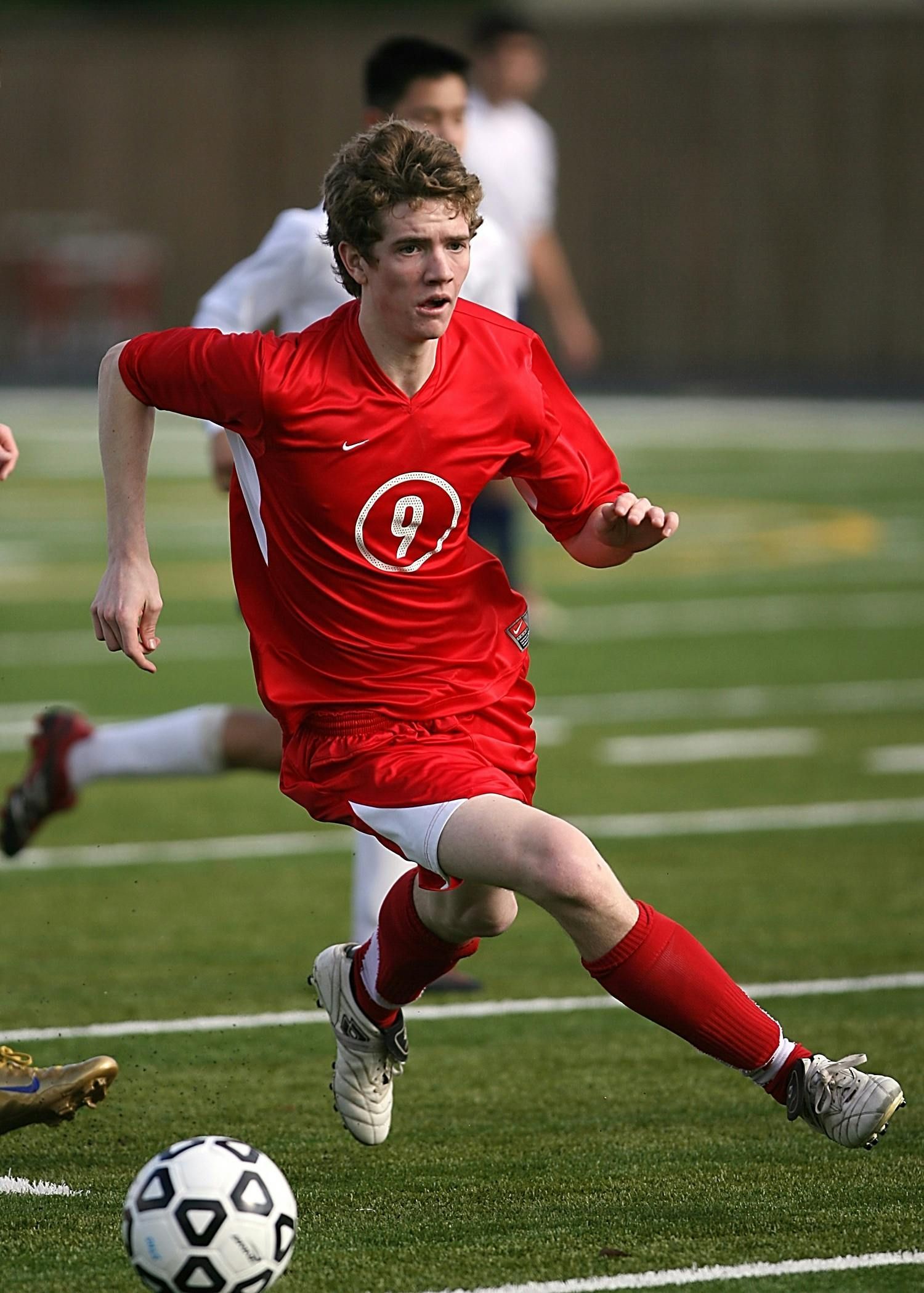 Soccer player in red jersey running on green field; the player is focused on the ball.