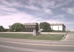 Small brick building and white hall in a grassy lot beside a road under a cloudy sky