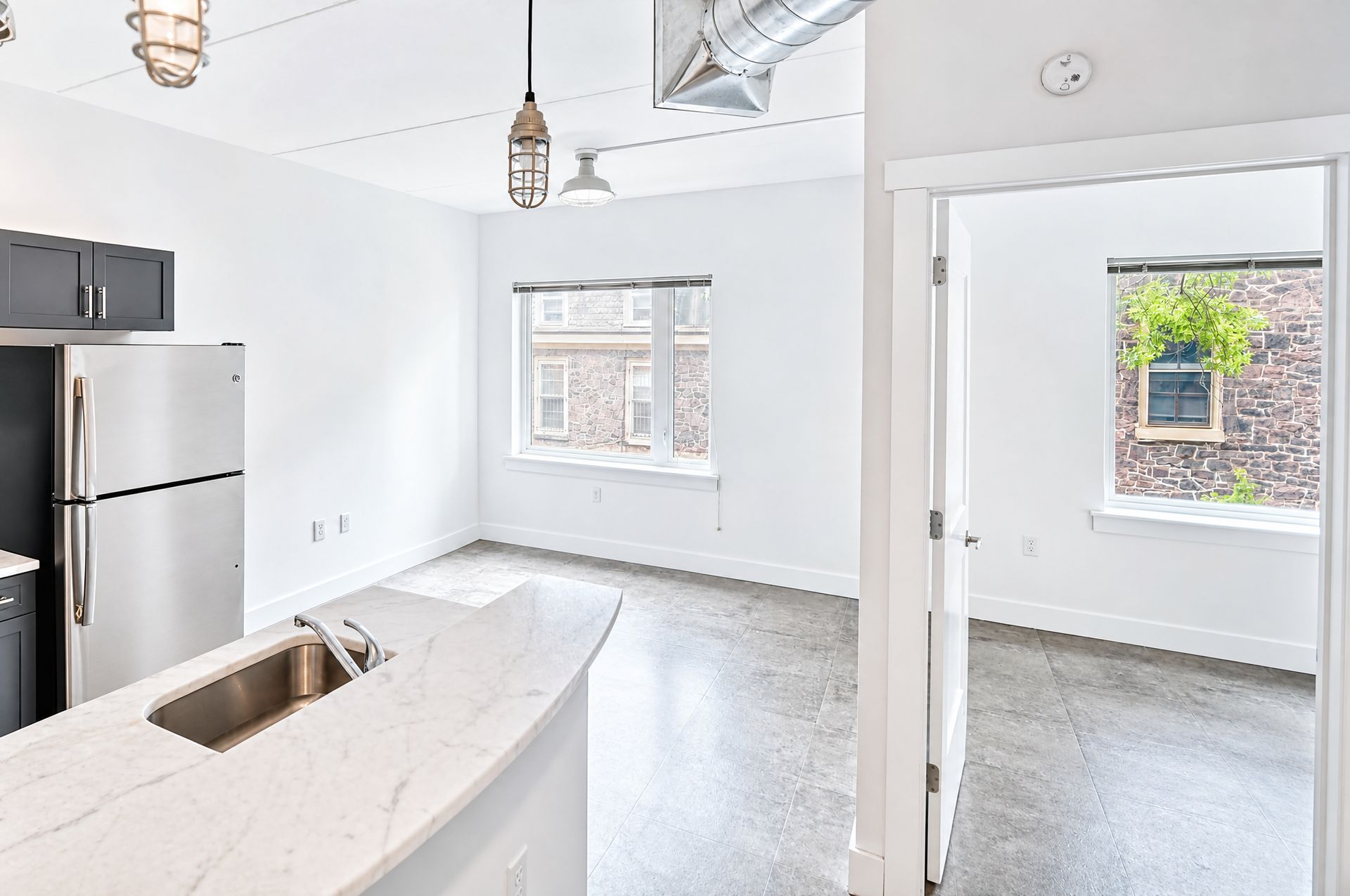 Bright white kitchen with island sink, stainless fridge, and open doorway to a small adjacent room.