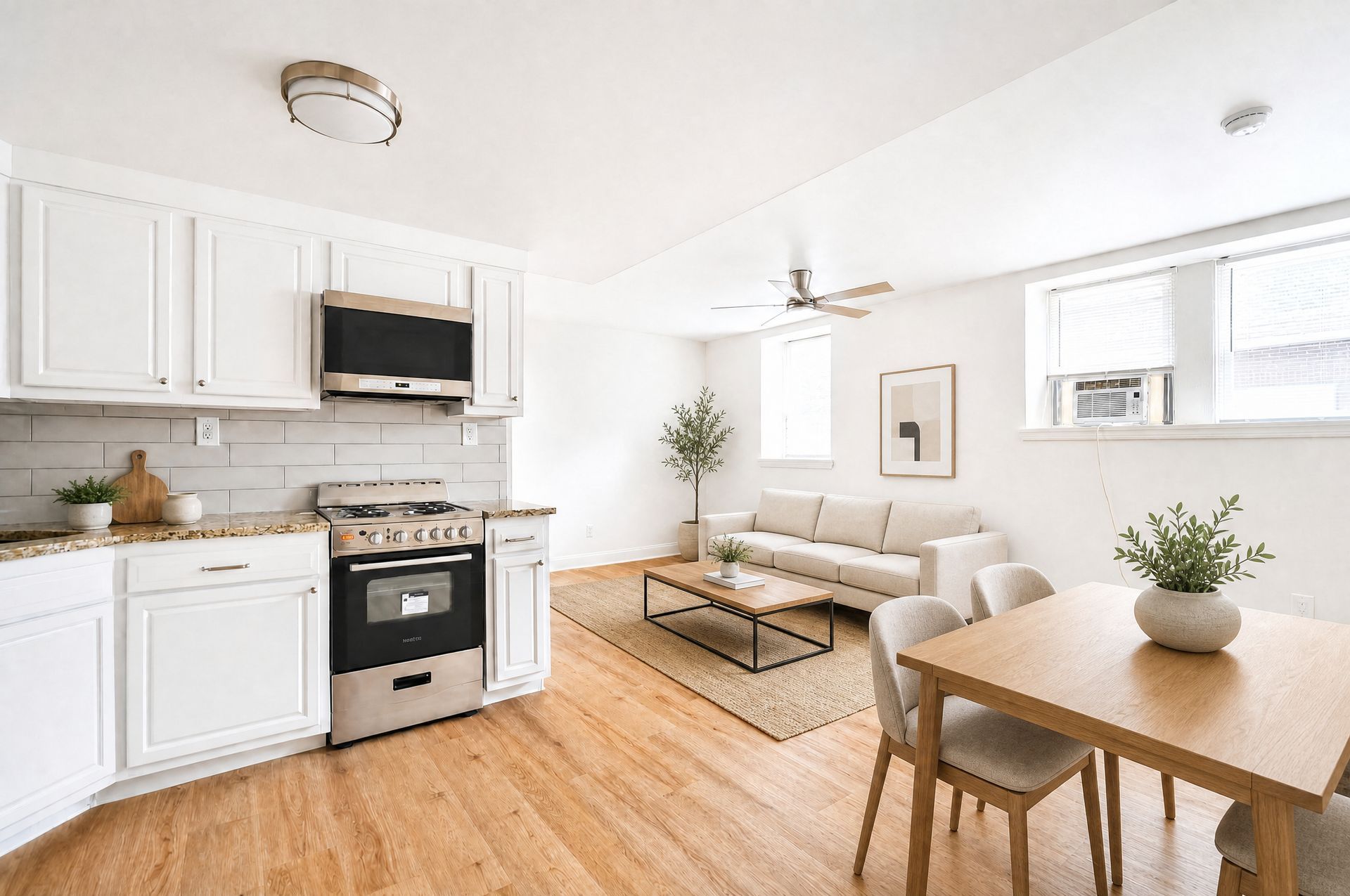 Bright white living room with kitchen, sofa, and dining table in a sunlit open-plan space