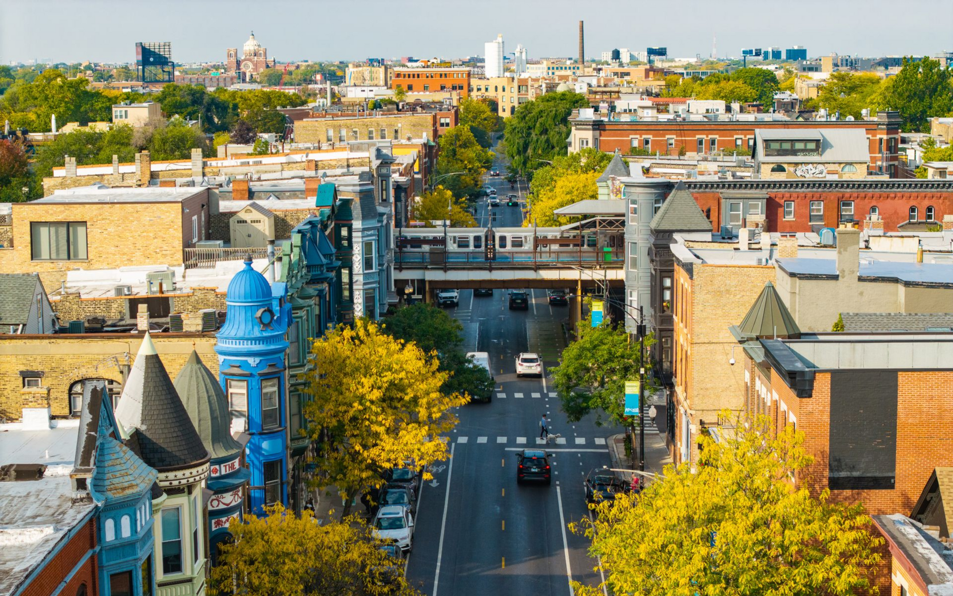 Aerial view of a city street lined with colorful buildings and autumn trees under a bright sky