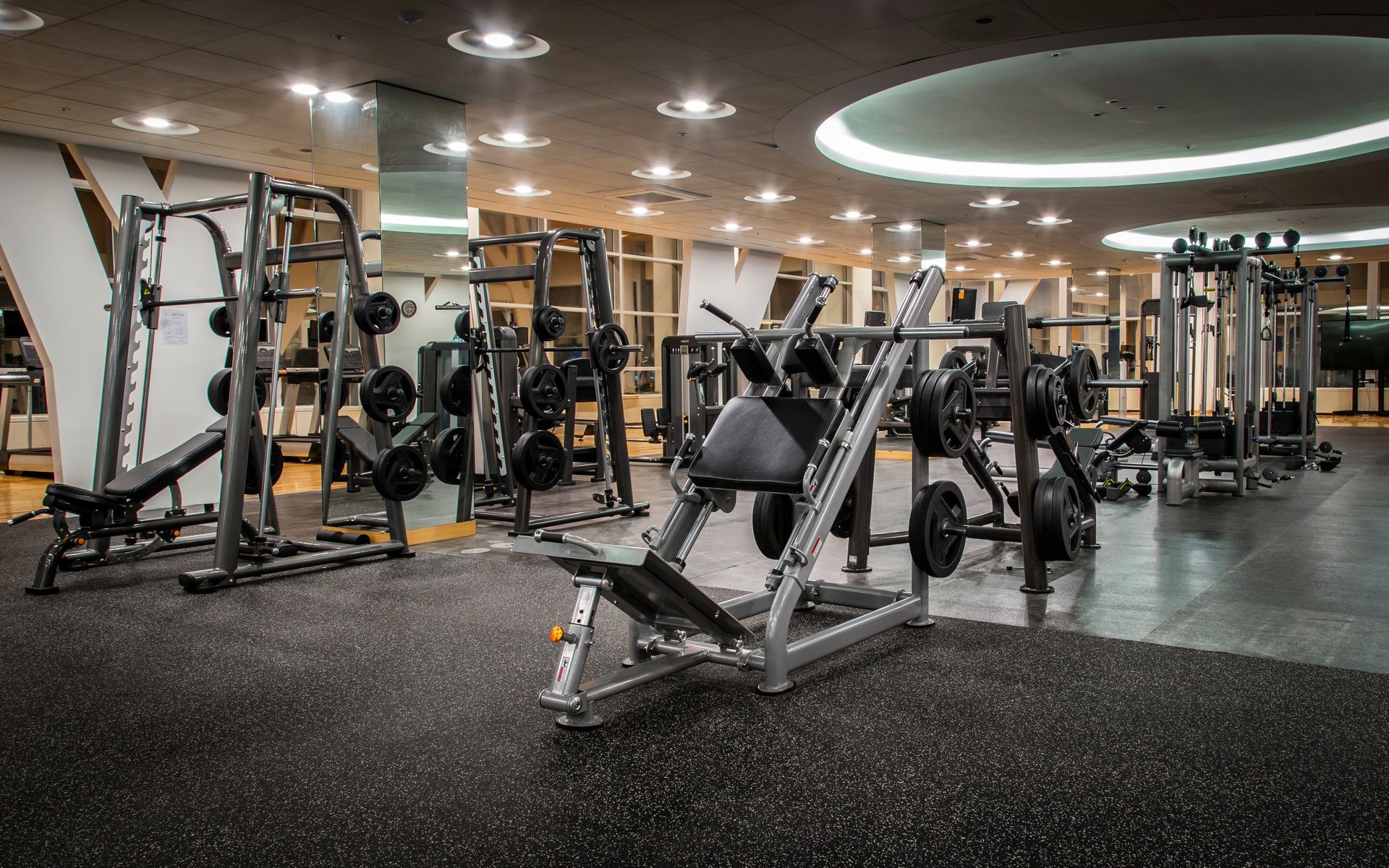 Empty gym with weight machines and benches under bright ceiling lights.