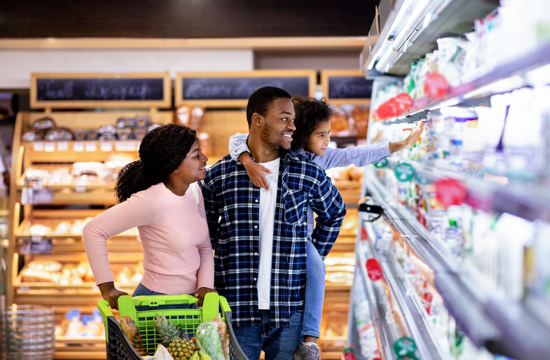 Three shoppers browse grocery shelves in a brightly lit supermarket aisle.