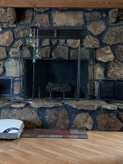 A stone fireplace in a living room with a wooden floor.