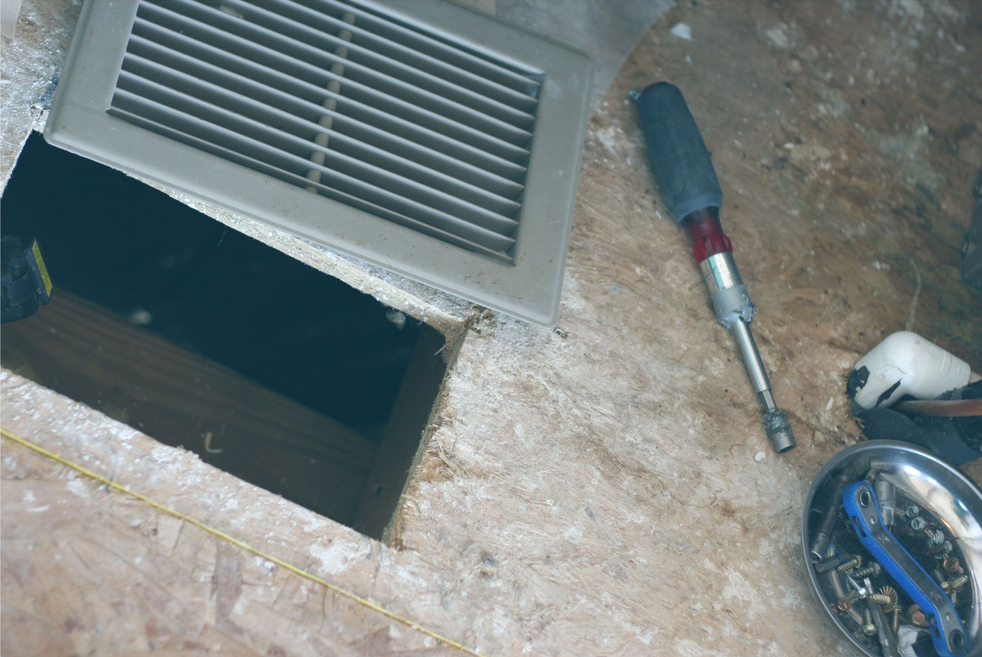 A screwdriver is sitting on the floor next to a vent.