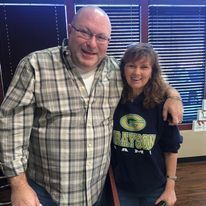 A man in a plaid shirt and a woman in a green bay packers shirt are posing for a picture.