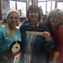 Three women are posing for a picture while one of them is holding a check.