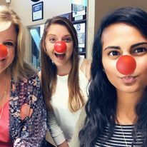 Three women wearing red clown noses are posing for a picture.
