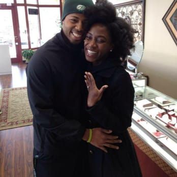 A man wearing a green bay packers hat is hugging a woman