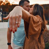 A man and woman are kissing while the woman shows off her engagement ring.