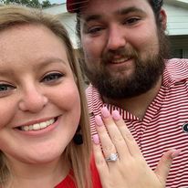 A man and a woman are posing for a picture together . the woman is wearing a ring on her finger.