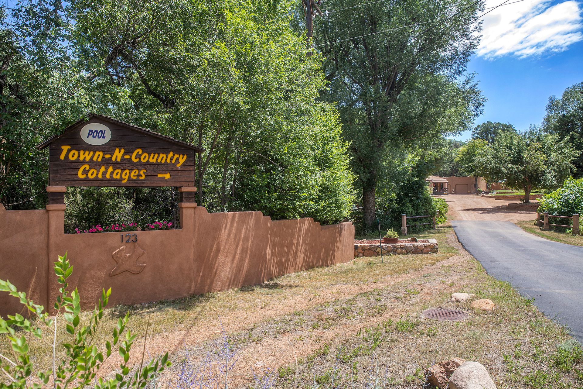 Sign for Town-N-Country Cottages beside a dirt road with brown wall and trees, bright sky.