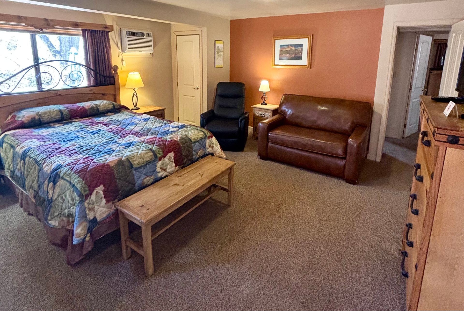 Bedroom with king bed, brown sofa, black recliner, wooden dresser, beige carpet, and orange wall.