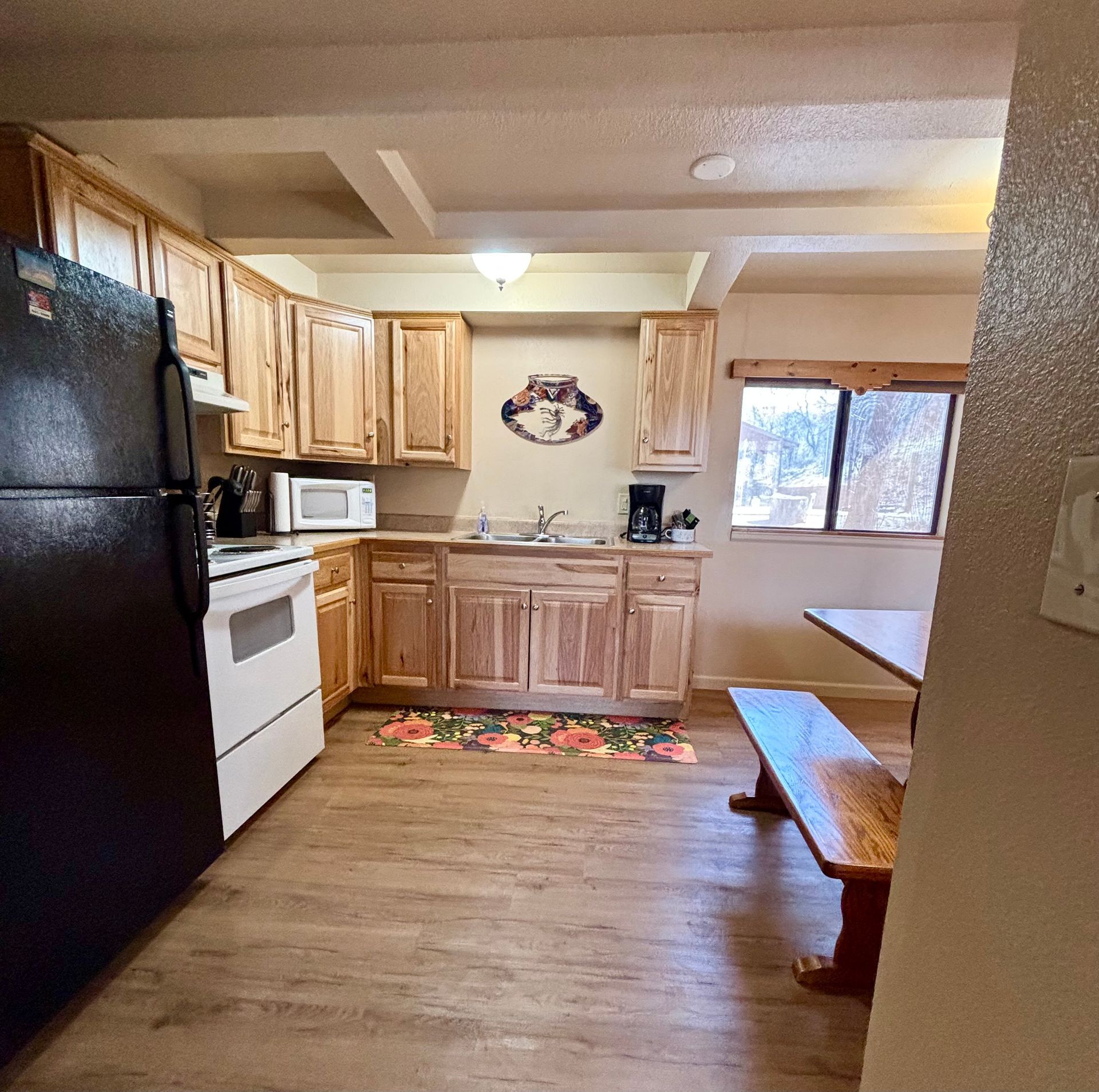 Kitchen with wood cabinets, black refrigerator, white oven, and a wooden table with a bench.