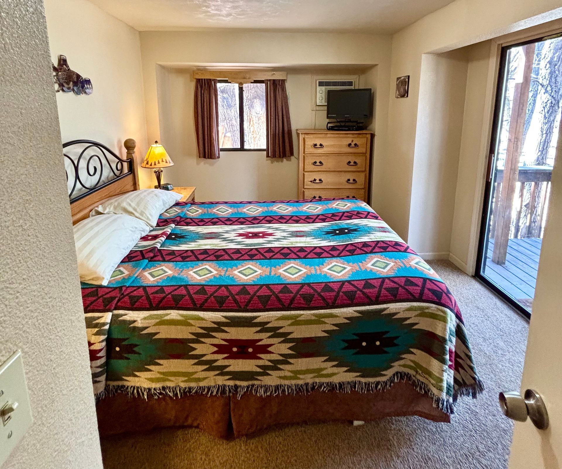 Bedroom with a bed, dresser, window, and sliding door to a balcony. Colorful patterned blanket on the bed.
